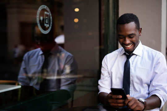 African businessman drinking coffee in cafe. Happy smiling man using the phone..