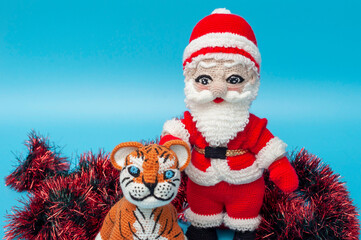 On a blue background there are knitted toys of Santa Claus and a tiger next to tinsel. Close-up.