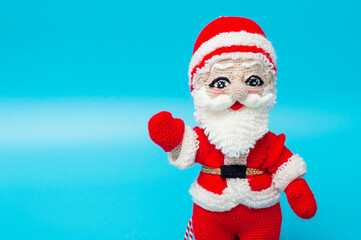 knitted Santa Claus toy waves his hand on a blue background. copy space.