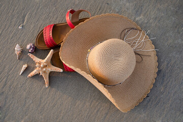 Flat lay photo of straw hat, red sandals and starfish with seashells sea sandy beach. Summer...
