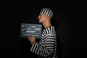 Mug shot of prisoner in striped uniform with board on black background, side view