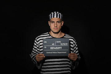Mug shot of prisoner in striped uniform with board on black background, front view