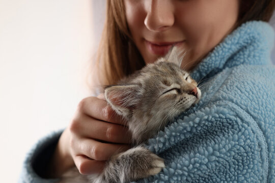 Woman with cute fluffy kitten against light background, closeup