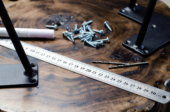 Roulette and pencil. Screws on the table in the workshop. The hands of a wood master. Metal table legs. Desktop. Working process. Furniture creation.