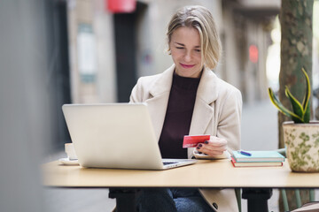 Middle age woman holding credit card and using laptop computer to do online shopping or internet banking, spending electronic money to buy present