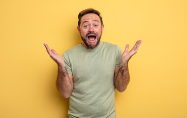 middle age handsome man feeling happy, excited, surprised or shocked, smiling and astonished at...