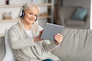 Smiling mature woman using tablet sitting on couch