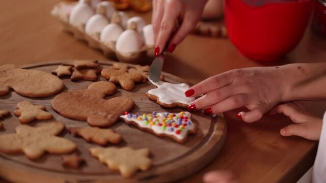 Hand of mom help daughter decorates gingerbread using white glaze. Christmas and New Year traditions concept. Christmas mood