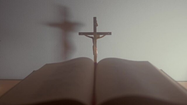 Close-up footage of the metal cross on a white background with the blurry Holy Bible in the foreground