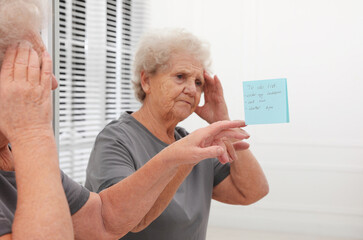 Fototapeta premium Senior woman looking at reminder note indoors. Age-related memory impairment