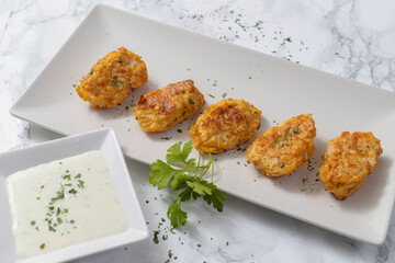 Rectangular white plate with vegetable nuggets accompanied by yogurt sauce with parsley leaves on...