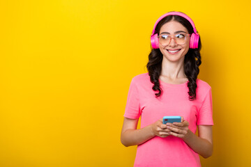 Photo of young lovely girl look empty space dreamy use smartphone earphones meloman isolated over yellow color background