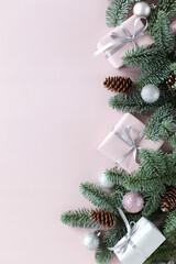 Christmas background, natural fir branches with decor, gift boxes, cones, Christmas toys on a pink background with copy space. flat lay, top view 