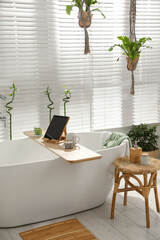 Stylish white tub and green houseplants in bathroom. Interior design