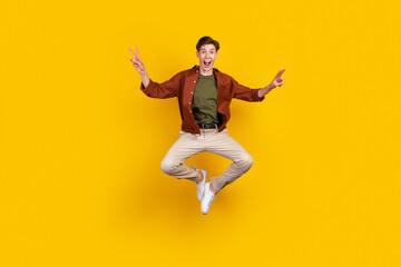 Full length photo of young cheerful man good mood jump show victory v-symbol isolated over yellow color background