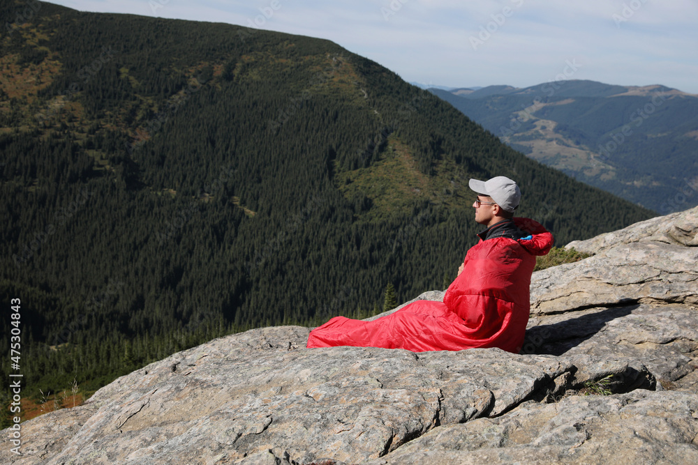 Wall mural tourist in sleeping bag on mountain peak