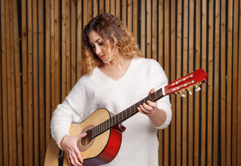 A beautiful woman plays a classical guitar, against the background of a wooden wall