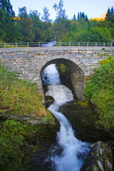 Historic stone bridge over part of the Stors&aelig;terfossen waterfall.  Beautiful views from Fosser&aring;sa hiking trail of . Close to Geiranger fjord, Norway. Summers day with clear blue sky over the scenery.