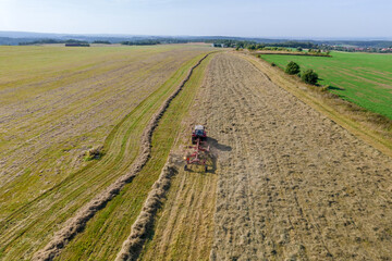 Aerial view on a tractor that collects hay in rows with a disc rake. Farmer stores fodder for cattle in summer season.