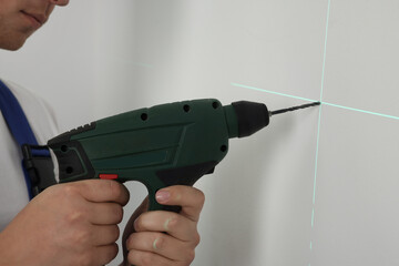 Man using cross line laser level for accurate measurement and drilling hole in light wall, closeup