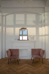 Comfortable armchairs placed near mirror with reflection and decorative elements in light spacious room with classic design and white wall