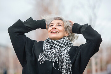 Portrait of a free, independent and happy mature woman in warm clothes against a gray autumn sky