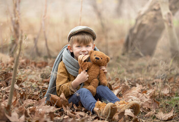 a boy in a vintage tweed cap and a knitted scarf and a yellow jacket and boots is sitting in nature...