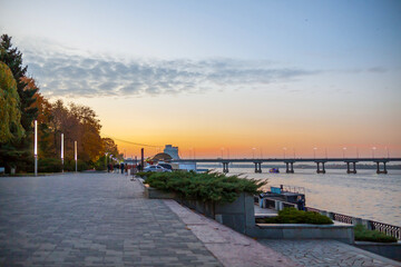River embankment in the evening, sky and bridge in the distance, empty sidewalk in the foreground for juices space text, blurred background