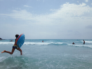 girl running in to the Mediterranean Sea with swimming mattress to catch the waves, Sardegna, Italy. People catching the waves, vacation.
