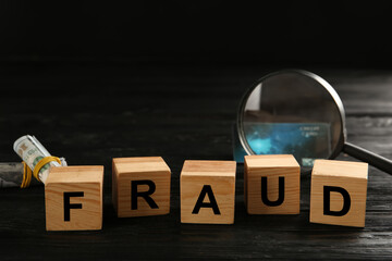 Wooden cubes with word Fraud near credit card, magnifying glass and money on black table, space for...