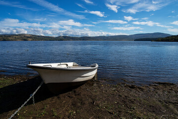 Fototapeta na wymiar A white old wooden boat anchored near the shore, in a secluded harbor. Landscape photography of a beautiful blue lake and an anchored white boat.