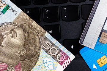 Polish 500 PLN banknote and credit cards arranged on the laptop keyboard. Cybersecurity of online...