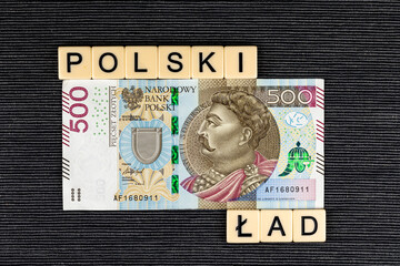 The sentence "Polski Ład" translated as  "Polish Order" and single Polish 500 PLN banknote on grey background.. New taxation rules in Poland. Photo taken under artificial, soft light