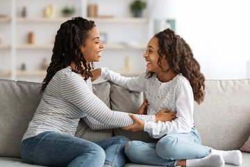 Happy african american mom tickling her laughing girl kid