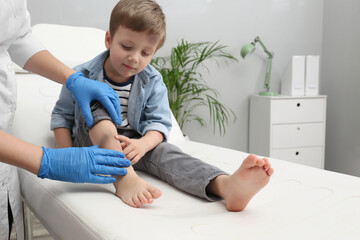 Doctor checking boy's leg with bruise at hospital - obrazy, fototapety, plakaty