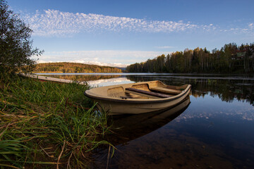 Obraz premium A white old wooden boat anchored near the shore, in a secluded harbor. Landscape photography of a beautiful blue lake and an anchored white boat.
