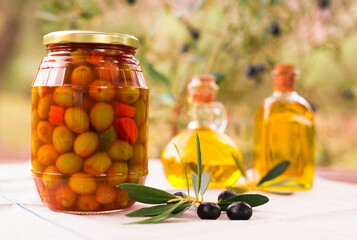 glass jar of pickled olives, oil and olives on table in an olive field