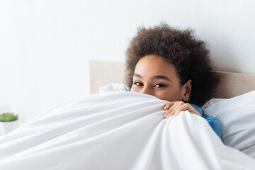 curly african american woman covering face with blanket