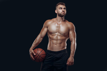 Fototapeta na wymiar Portrait of a very muscular naked man playing basketball isolated on black background