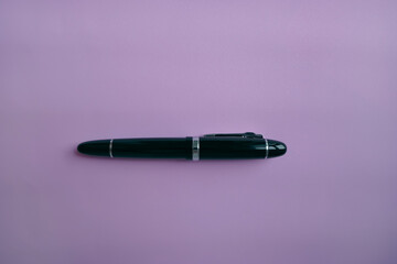 close up of a black fountain pen on textured light pink background