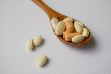 vitamins in a wooden spoon, tablets and pills in a spoon. medicines are on the table. pills on a white background