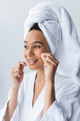 cheerful young african american woman in bathrobe flossing teeth in bathroom