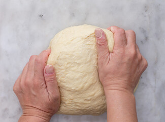 Top view of woman hands kneading bread dough on marble surface by hand