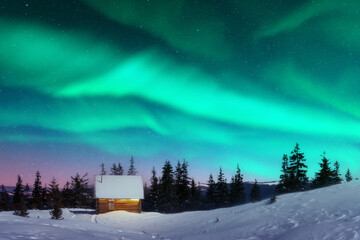 Fantastic winter landscape with wooden house with light in window in snowy mountains and northen light in night sky. Christmas holiday and winter vacations concept