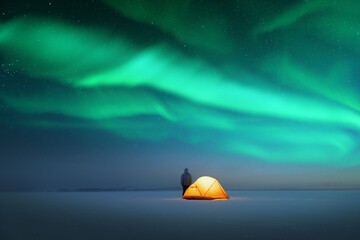 Tourist near yellow tent lighted from the inside against the backdrop of incredible starry sky with...