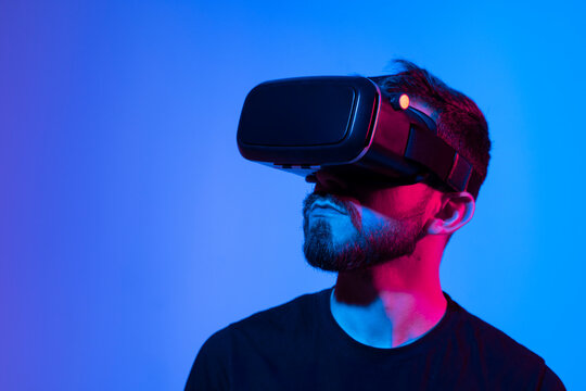 Portrait of man using VR headset while playing a video game in dark interior illuminated neon light. Close-up futuristic googles with colored light. - Powered by Adobe