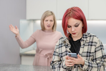 Angry woman scolds her teenage daughter, girl uses smartphone and ignores her mom. Family relationships