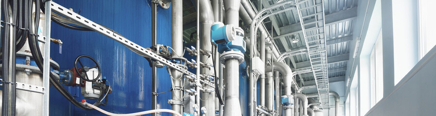 Large industrial water treatment and boiler room. Shiny steel metal pipes and blue pumps and...