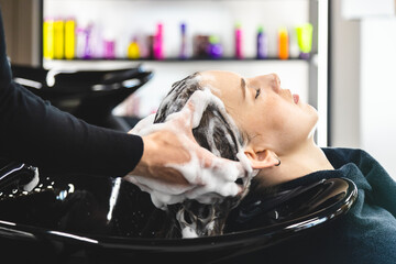 Master woman hairdresser gently washes the girl's hair with shampoo and conditioner before styling in a beauty salon.