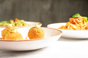 Delicious dishes of Italian gastronomy on white marbled board and gray background. Arancini Siciliana, pasta bolognese and spaghetti with pesto. Copy space. High quality photo